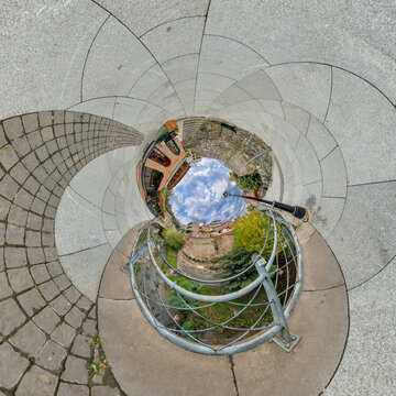 creative tiny planet photo of a rural landscape with dirt road, green fields, and cloudy sky forming a circular world.