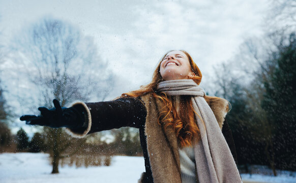 Redhead woman reaches for snow in a winter coat outdoors