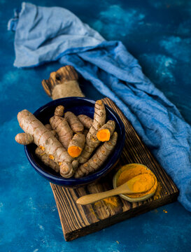 Fresh turmeric roots and turmeric powder on wooden board