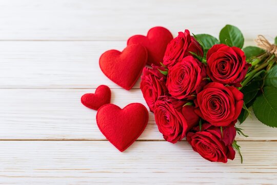A bouquet of red roses and plush hearts rests on a white wooden surface.