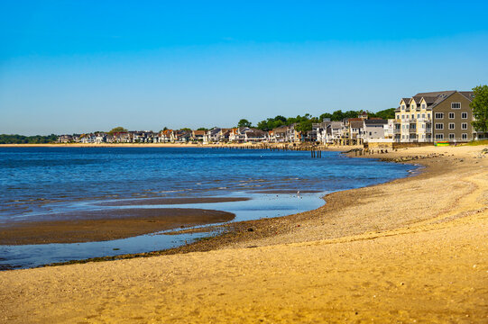Waterfront homes at Walnut Beach in Milford, Connecticut, with sandy shoreline, calm Long Island Sound water, and a clear blue summer sky.