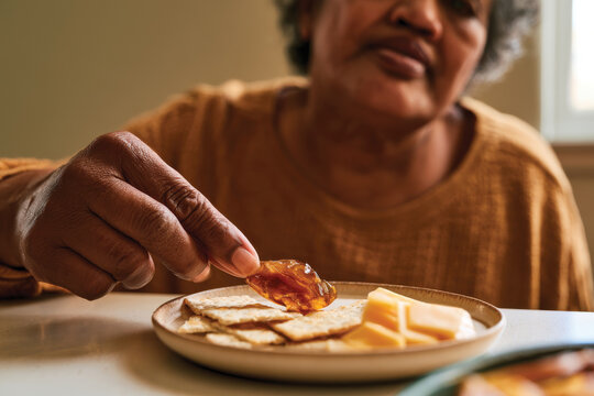 A heartwarming image of an elderly woman enjoying crackers topped with a delicious jam, embodying comfort, warmth, and simple pleasures of life shared over food moments.