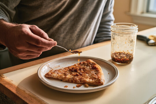 Close-up of a person adding spicy sauce on a slice of pizza, showcasing the joy of customizing comfort food to enhance flavor and personal preference.