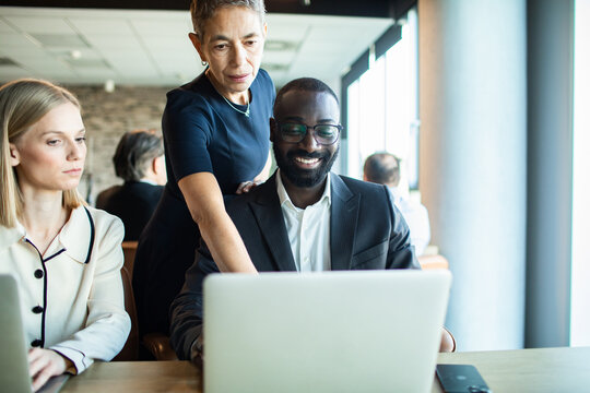 Senior colleague guiding coworker on laptop in office