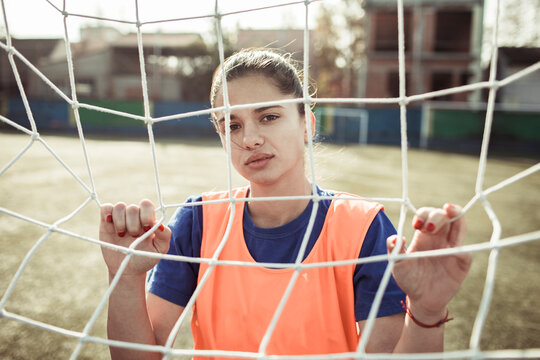 Young woman soccer player gripping goal net