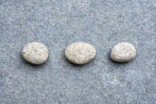 Three smooth pebbles arranged on a grey stone surface