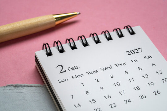 February 2027 - small spiral desktop calendar against art paper abstract, time and business concept