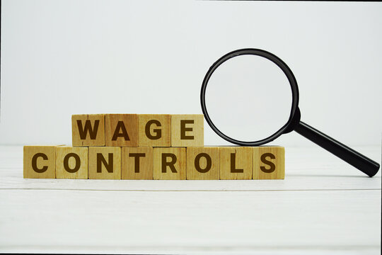 WAGE CONTROLS alphabet letters with magnifying glass on wooden background