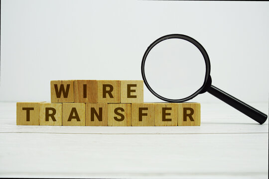 WIRE TRANSFER alphabet letters with magnifying glass on wooden background