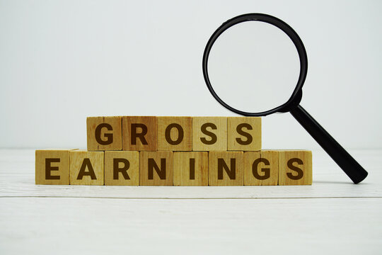 GROSS EARNINGS alphabet letters with magnifying glass on wooden background