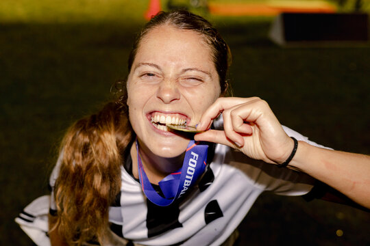 Female football champion biting gold medal after winning night final