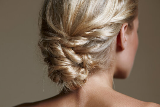 rear view of a young woman with beautiful blonde hair styled in an intricate braided updo for a wedding or formal evening event against a neutral studio background